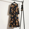 Dunkelblaue Maxi-Kleid mit Blumenmuster auf einem Haken vor einer weißen Wand.
