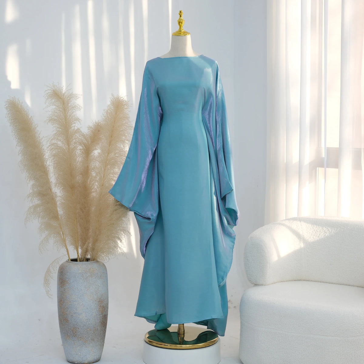 Türkisfarbenes Kaftankleid mit Schmetterlingsärmeln auf einem Mannequin neben getrocknetem Pampasgras.