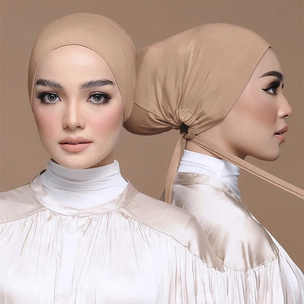 A woman wearing a beige elegant modal hijab turban cap and white blouse.