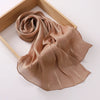 Un châle fluide, crinklé et brillant de couleur brun clair drapé dans un cadre en bois.
