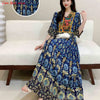 Eine Frau modelliert ein blau-gelbes, besticktes Maxi-Kleid im Boho-Stil mit goldenen Akzenten.