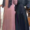 Eine Frau in einem langen, fließenden mauvefarbenen Kaftan-Abaya mit schwarzem Hijab und eine Frau in einem schwarzen Kaftan-