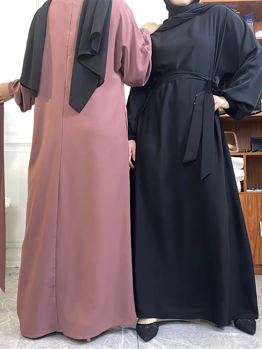 Eine Frau in einem langen, fließenden mauvefarbenen Kaftan-Abaya mit schwarzem Hijab und eine Frau in einem schwarzen Kaftan-