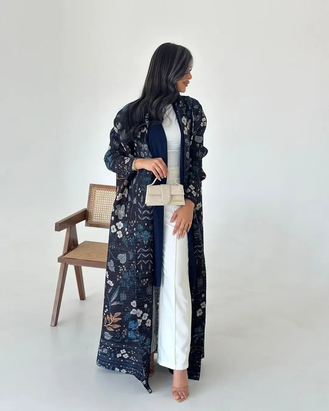 Une femme portant un trench-coat à manches longues à plissé bleu foncé par-dessus une robe blanche.