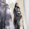 Eine Frau in einem grauen Blumenabaya und Hijab in einer Ganzkörperaufnahme.