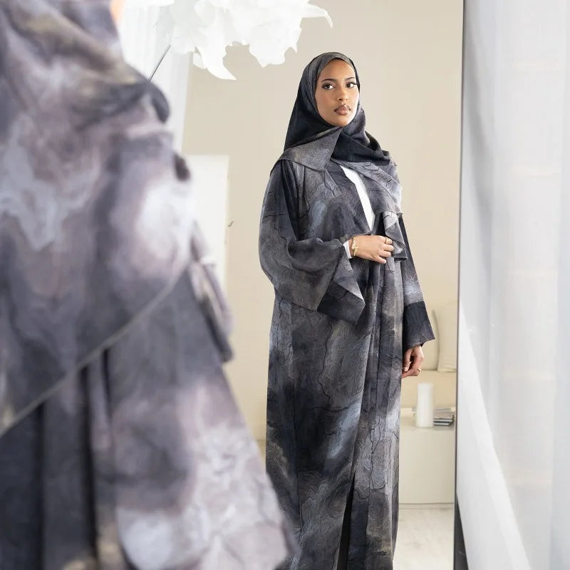 Eine Frau in einem grauen Blumenabaya und Hijab in einer Ganzkörperaufnahme.