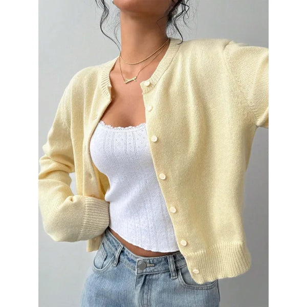 A woman wearing a pale yellow knit cardigan sweater over a white top and blue jeans.