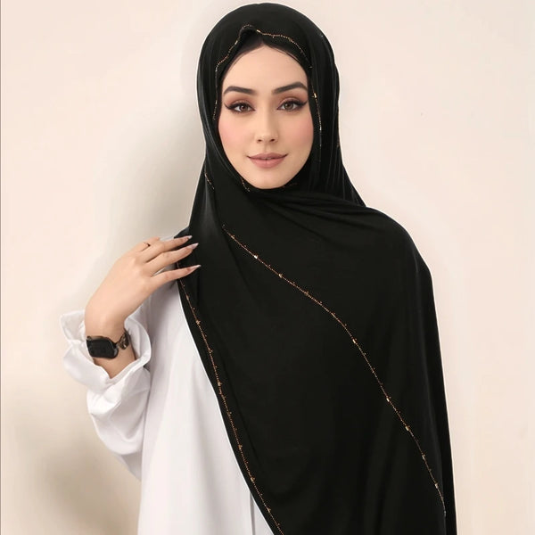 A woman wearing a black glitter shimmer edge cotton jersey hijab scarf over a white top.