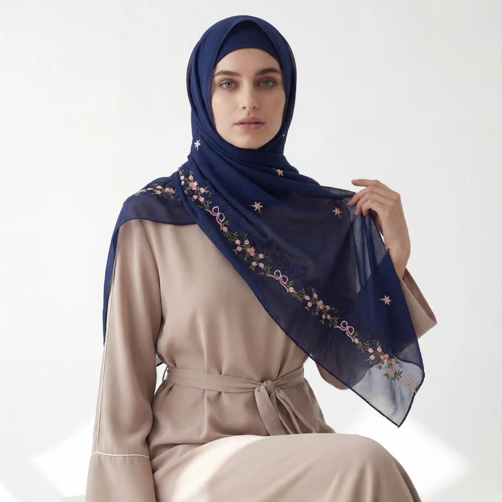 A woman wearing a navy blue chiffon hijab with floral embroidery and a beige top.