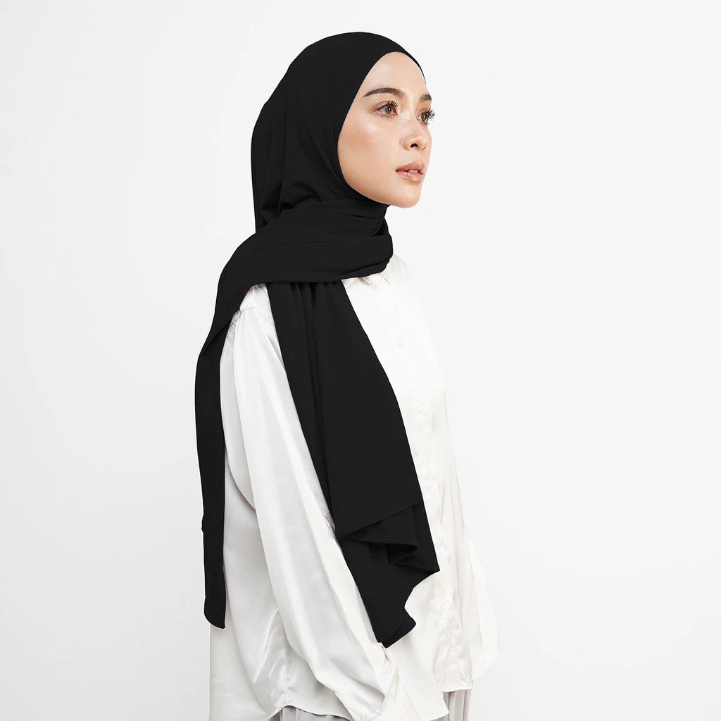 Eine Frau trägt einen schwarzen Instant-Hijab-Schal über einem weißen Oberteil.