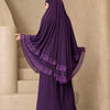 Eine Frau in einem lila, mehrlagigen Spitzen-Khimar-Abaya-Set steht neben Steinstufen.