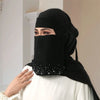 Eine Frau trägt einen eleganten schwarzen Niqab-Hijab mit floraler Diamantverzierung und einem weißen Oberteil.