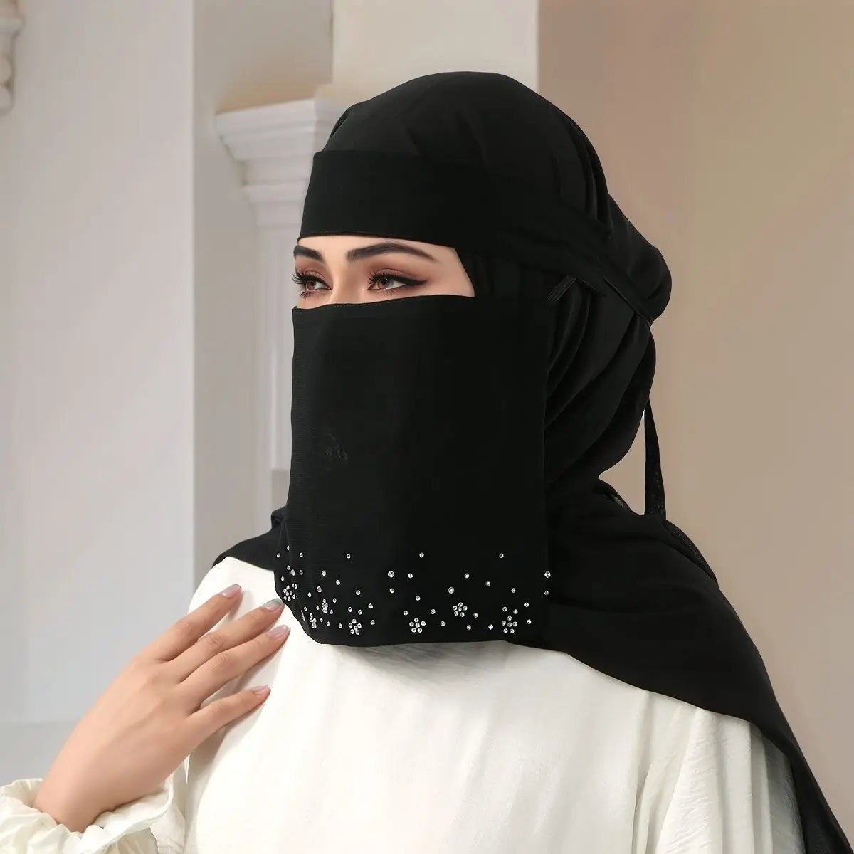 Eine Frau trägt einen eleganten schwarzen Face-Veil-Hijab mit Blumen-Diamantverzierung und einem weißen Oberteil.