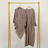 Beige, elegante Abaya und Khimar-Set auf goldener Kleiderstange vor weißem Hintergrund.