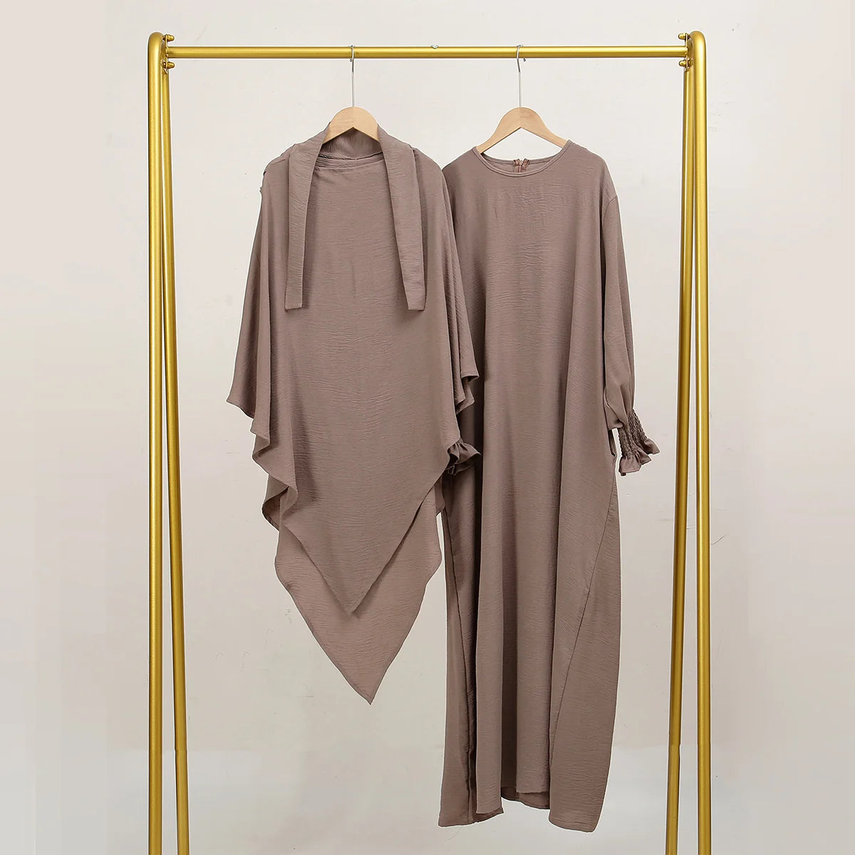 A beige two-piece abaya and khimar set displayed on a gold hanger against a white background.