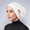 Eine Frau trägt eine beige Jersey-Baumwoll-Hijabkappe und ein schwarzes Rollkragenoberteil.