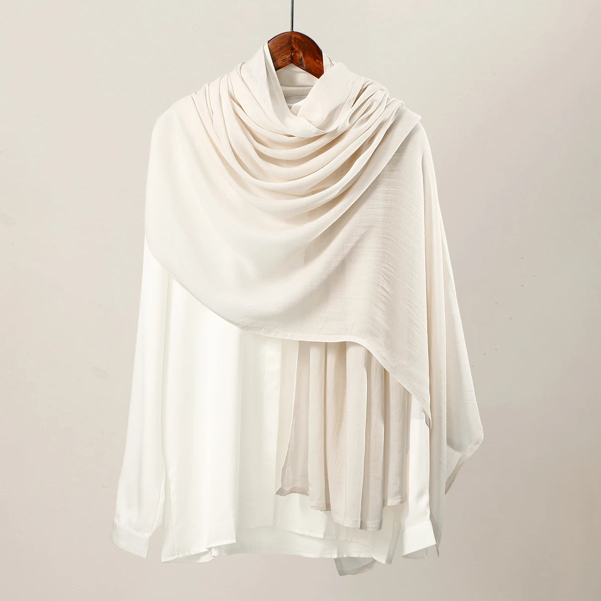 Pañuelo de hijab modal blanco grande y sólido colgado en una percha de madera.