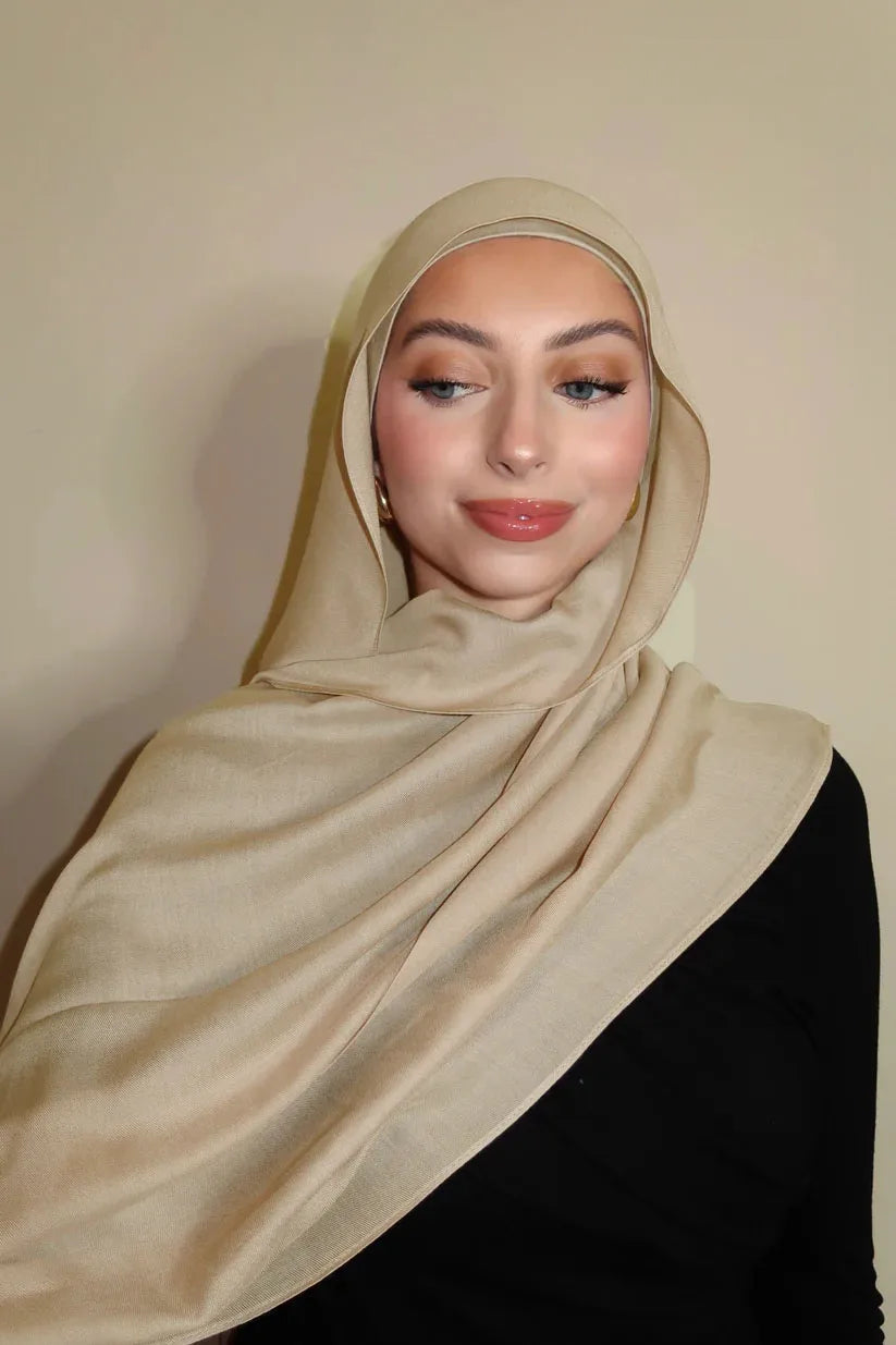 Eine Frau trägt einen beige-gradienten Rayon-Modal-Hijab und schwarze Kleidung.