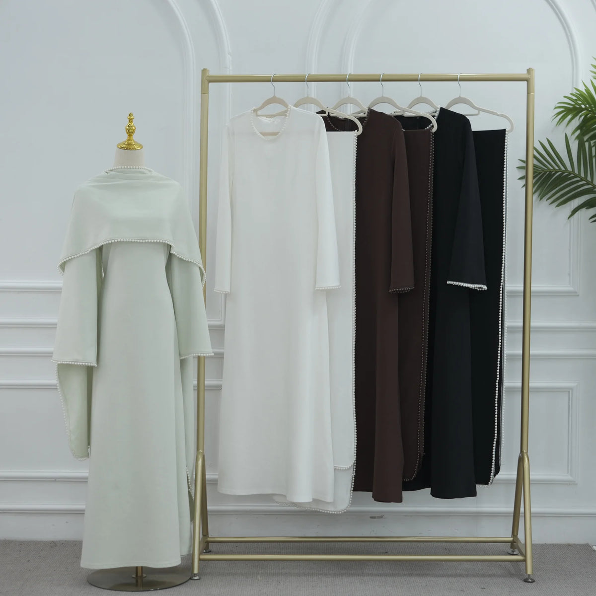 Langes, cremefarbenes, einfaches Abaya-Kleid auf goldener Kleiderstange in einem minimalistischen Kleiderständer.