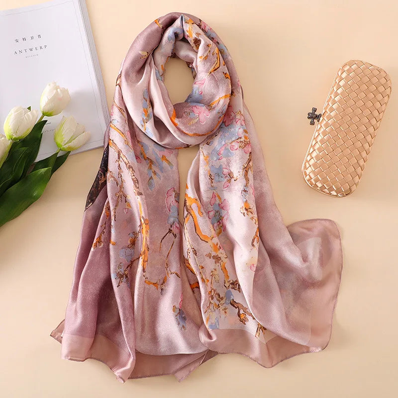 Fließendes, staubrosa Seidapareo-Schal mit Blumenmuster neben einer weißen Blume und einer goldenen Clutch