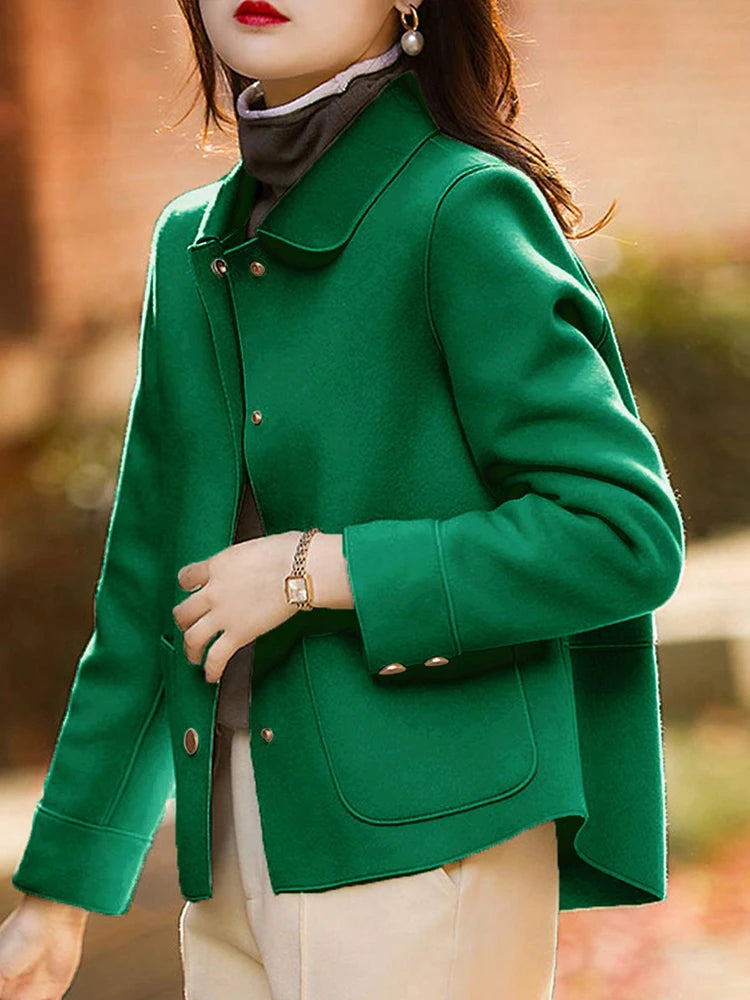 Une femme portant un manteau en laine vert émeraude par-dessus un haut de couleur claire.
