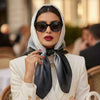 Une femme portant un foulard noir, des lunettes de soleil et un blazer blanc.