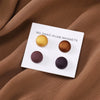 Eine weiße Karte mit fünf runden magnetischen Hijab-Pins in verschiedenen matten Farben vor einem braunen Stoffhintergrund.