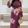 Modelin trägt ein langes, dunkles Pflaumen-Abaya-Kleid mit rosa und blauen Blumenmustern, steht drinnen.