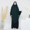 Eine Frau mit einem dunkelgrünen, zweilagigen Chiffon-Niqab und schwarzer Kleidung vor weißem Hintergrund.