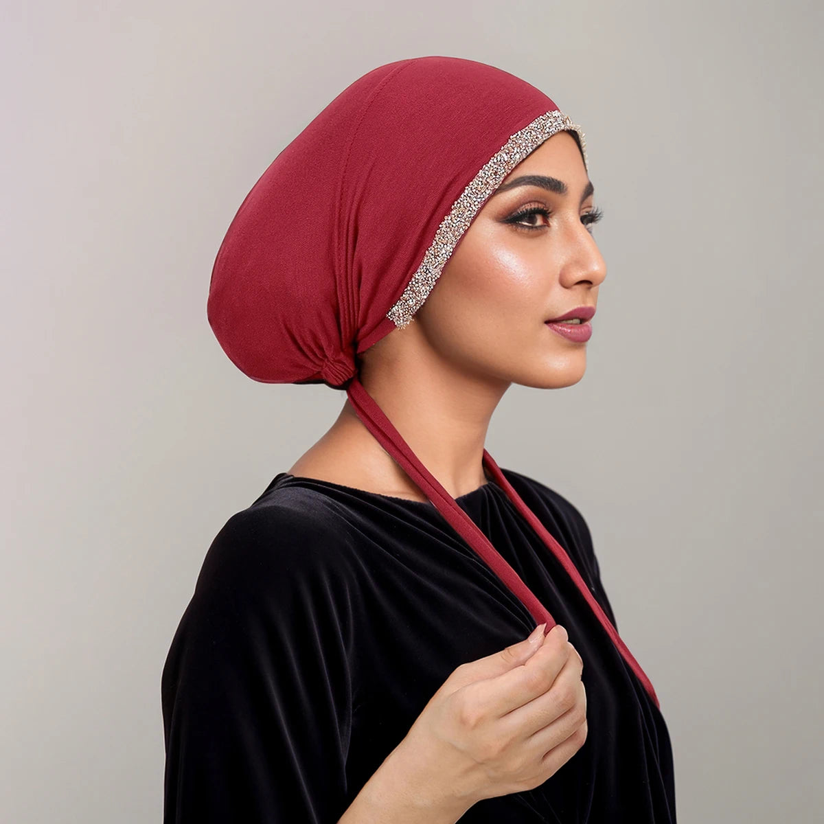 Eine Frau trägt einen tiefroten gekräuselten Hijab mit Strassverzierung und ein schwarzes Samt-Oberteil.