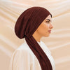 A woman wearing a solid brown turban hijab cap and white top, shown in profile.