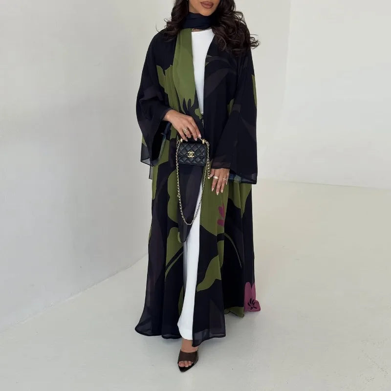 Una mujer vistiendo un conjunto de abaya de gasa negra y verde oliva con niqab negro y joyería dorada.