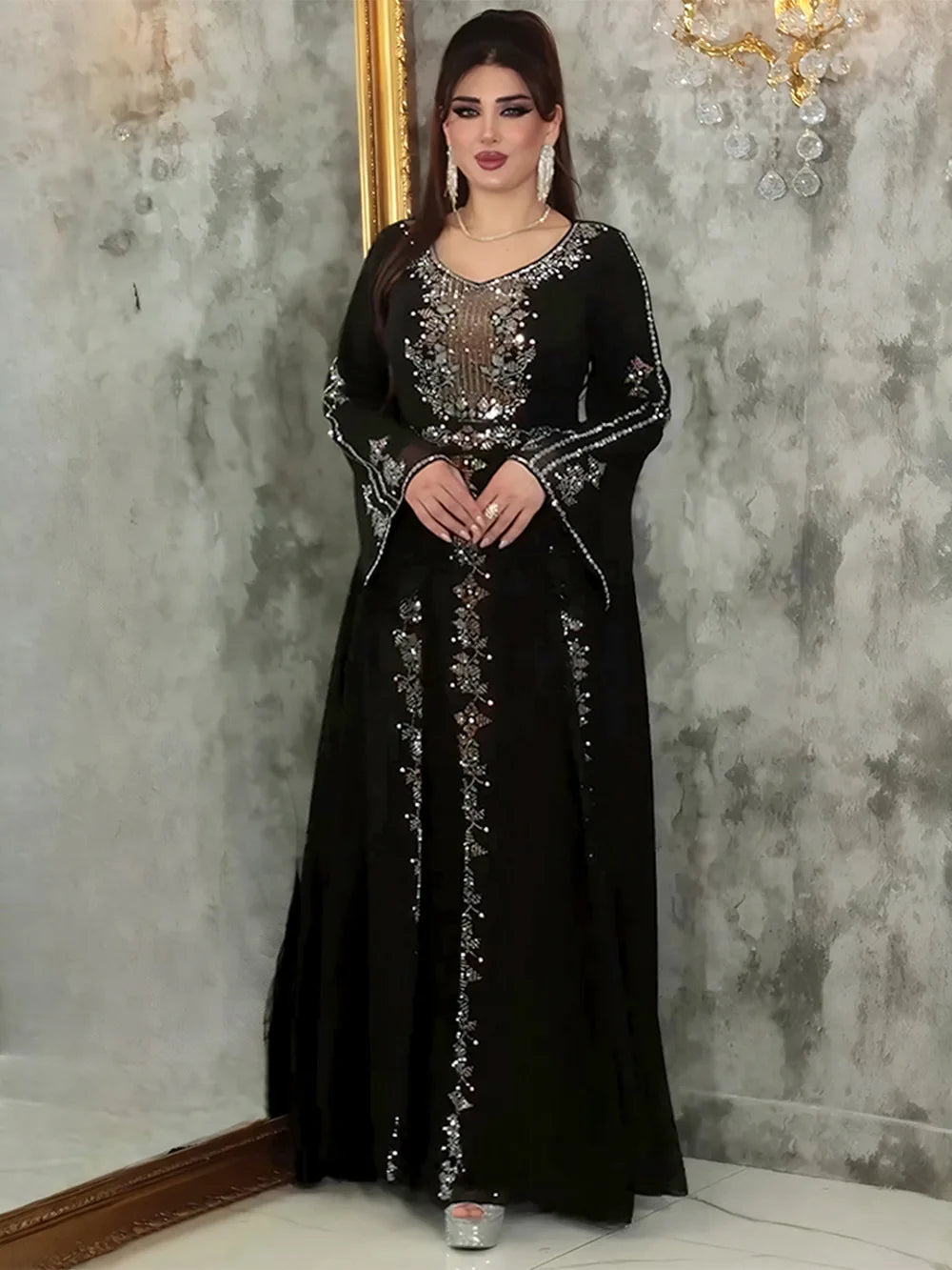 Eine Frau trägt ein elegantes schwarzes Abaya-Kleid mit durchscheinenden Rüschenärmeln und silbernen Verzierungen.