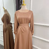 Beige, fließendes, langes Abaya-Kleid auf einem Mannequin mit einer goldenen Brosche.
