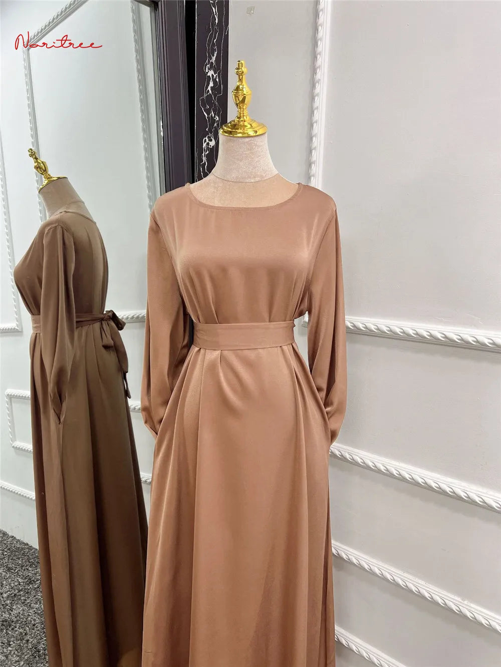 Beige, fließendes, langes Abaya-Kleid auf einem Mannequin mit einer goldenen Brosche.