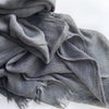 Foulard hijab en coton viscose gris doux, drapé et plié sur une surface blanche.