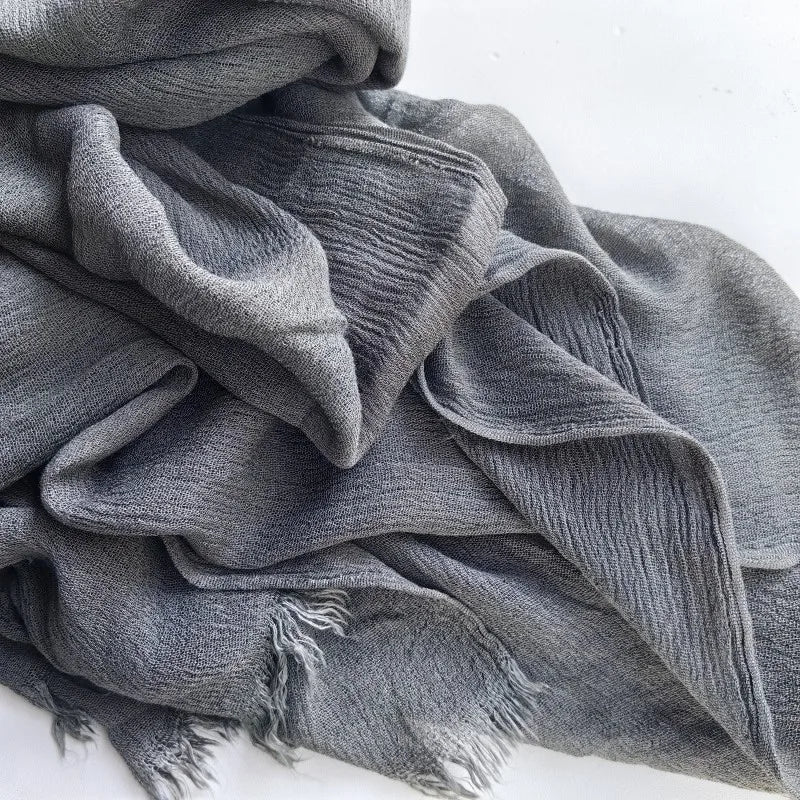 Foulard hijab en coton viscose gris doux, drapé et plié sur une surface blanche.