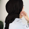Una mujer vistiendo un hijab de jersey de algodón instantáneo negro y una camisa azul claro, vista de lado.