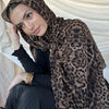 Una mujer vistiendo un hijab de estampado de leopardo marrón y ropa negra, mirando hacia abajo.
