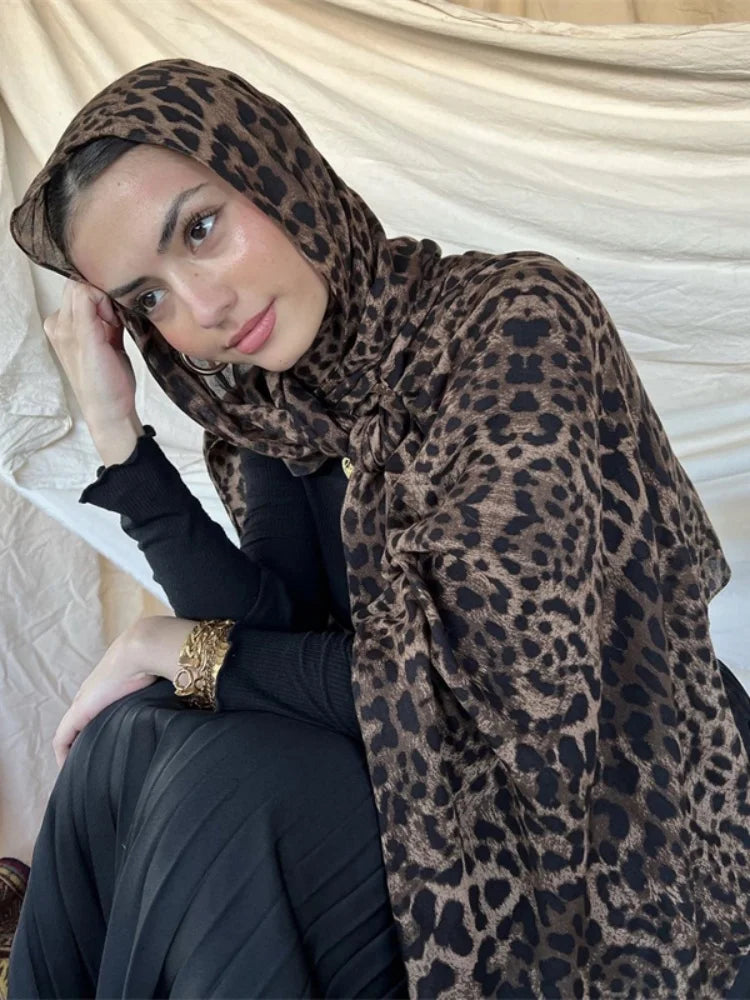 Una mujer vistiendo un hijab de estampado de leopardo marrón y ropa negra, mirando hacia abajo.