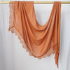 Hijab de encaje naranja quemado y fluido, colgado en un perchero dorado.