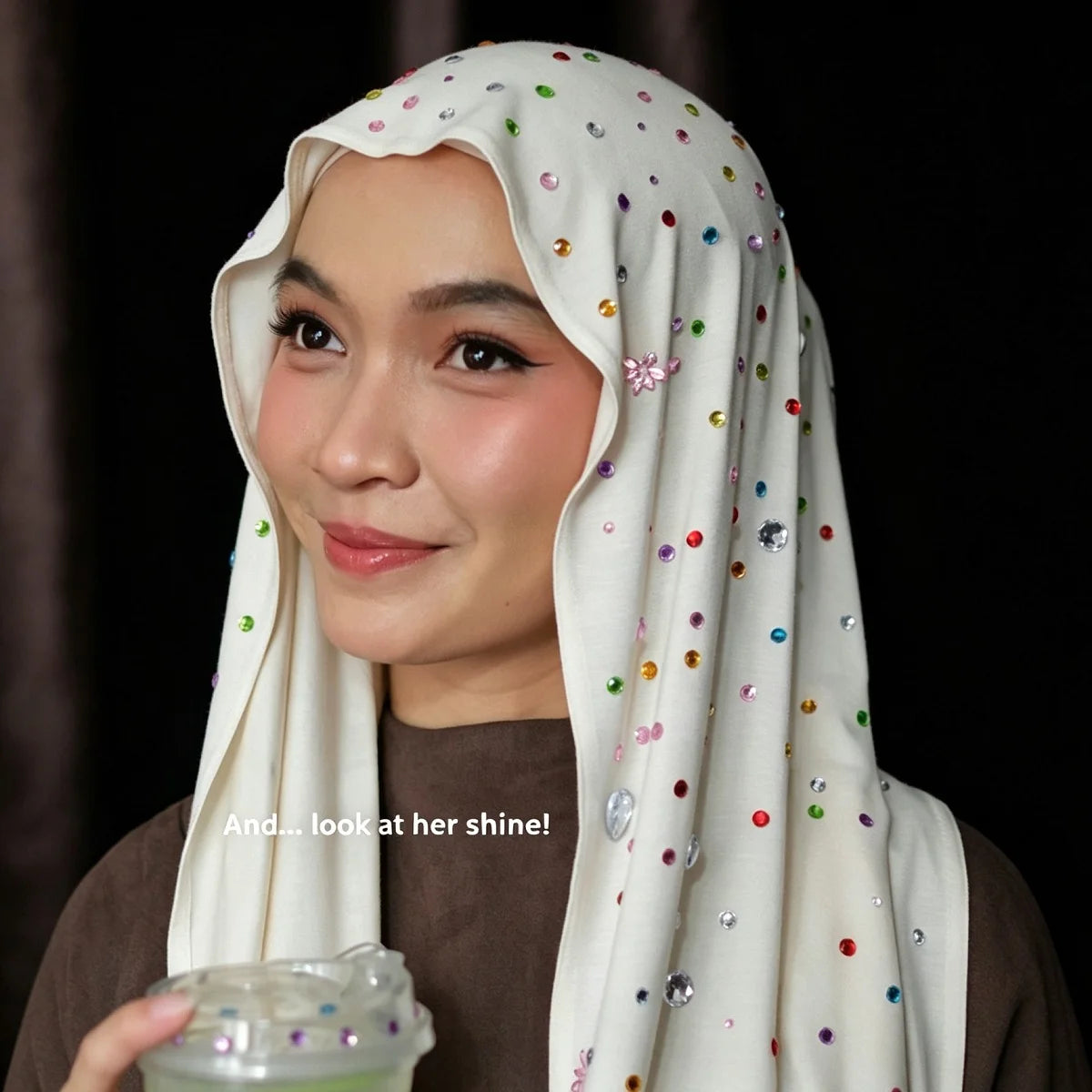 A woman wearing a white hijab adorned with colorful sequins and beads, smiling slightly.