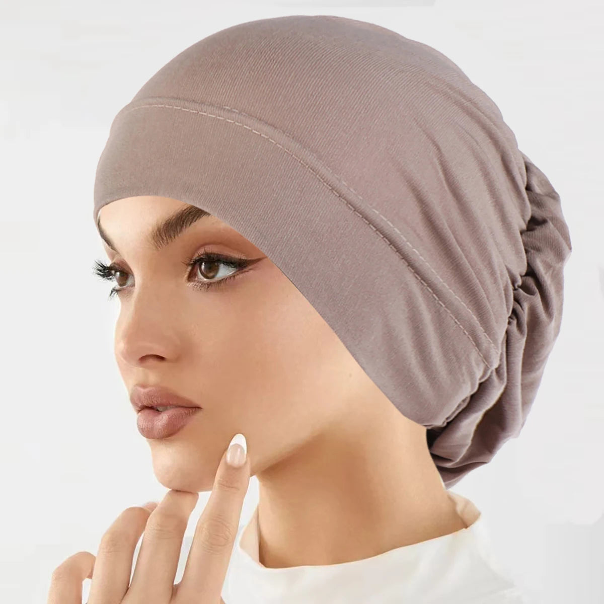 Nahaufnahme einer Frau mit beige-Stretch-Turban, die ihr Gesicht berührt.