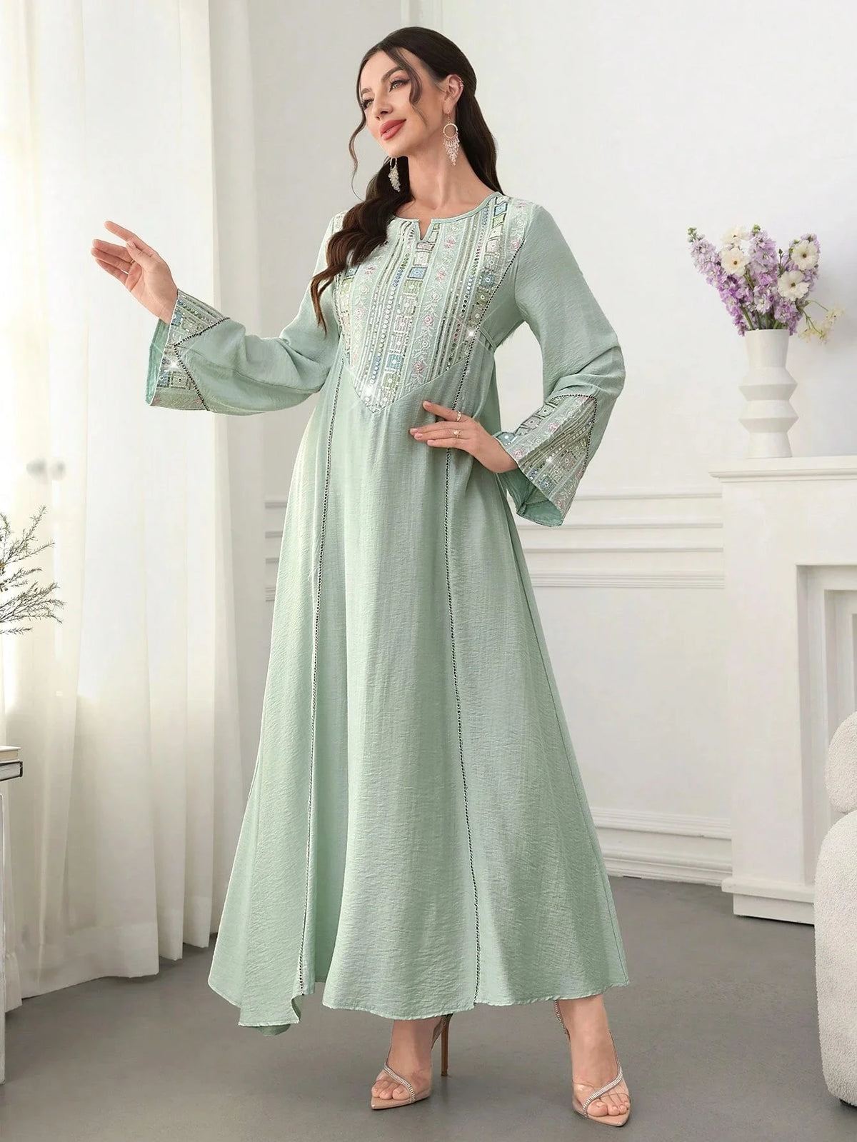 Eine Frau präsentiert eine hellgrüne, mit Pailletten bestickte Abaya mit langen Ärmeln und fließendem Rock.