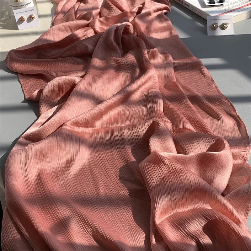 Fließender, staubrosa Crinkle-Satin-Chiffon-Hijab elegant in Sonnenlicht drapiert.