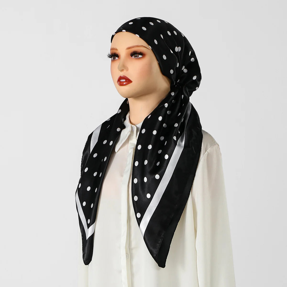 Eine Frau modelliert einen schwarzen Polka-Dot-Seiden-Instant-Hijabschal mit weißen Streifen vor hellem Hintergrund.