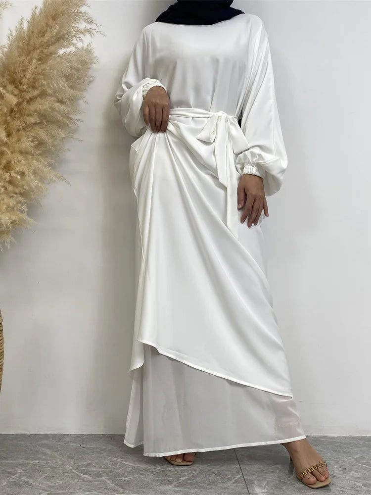Eine Frau in einem weißen marokkanischen Kaftan-Abaya mit schwarzem Hijab vor hellem Hintergrund.