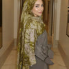 A woman wearing an elegant olive green watercolor print modal scarf and a matching coat in a hallway.