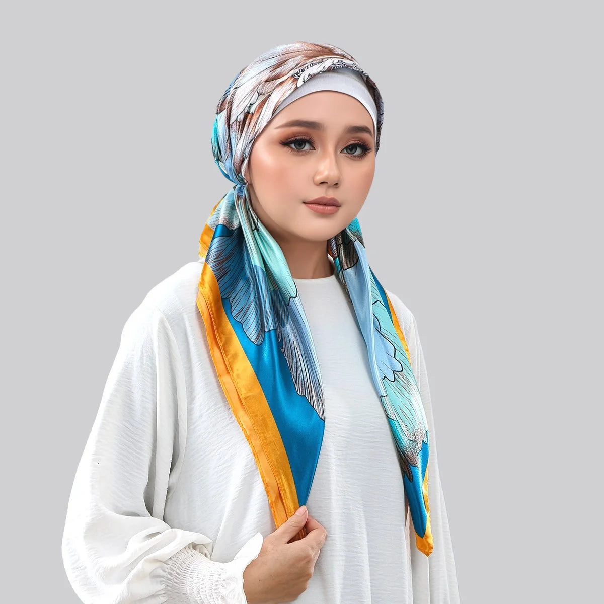 Une femme portant un foulard instant en satin bleu et or autour de sa tête et de son cou.