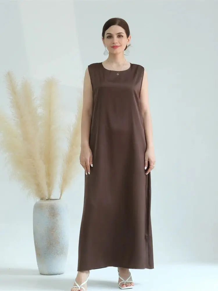 A woman models a long, flowing brown modest abaya dress against a light background.